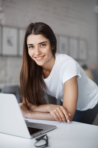 Portrait of beautiful caucasian woman using laptop computer standing in open space coworking centre looking for new job looking at camera smiling. - 写真・画像