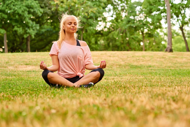 Young woman meditating on a field in a park - Фото, зображення
