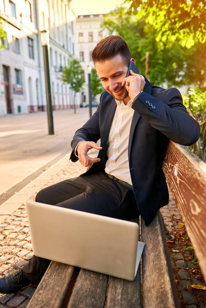 Young businessman siting on a bench with his laptop and talking  - Foto, immagini