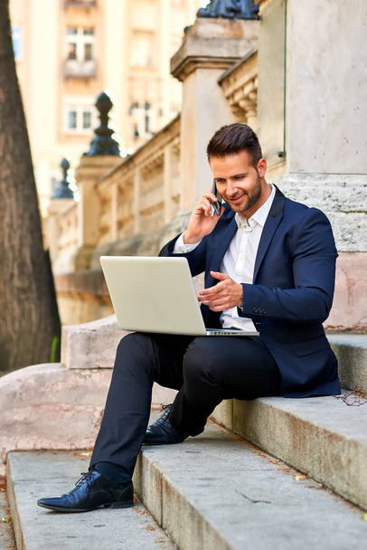 Young businessman siting on the stairs with his laptop and talki - Foto, Imagen
