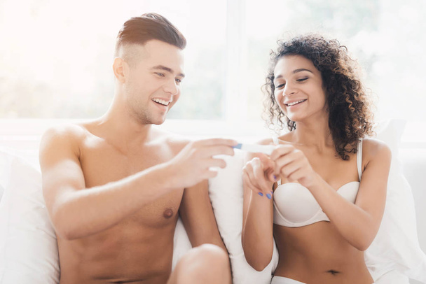 Young couple sitting on bed and looking at pregnancy test girl. They are happy and smiling. - Foto, Bild