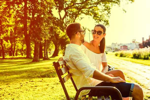 Beautiful young couple relaxing on a sunny summer day on a bench - 写真・画像