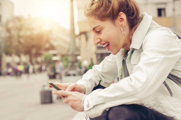 Happy woman sitting on street, typing message, chatting on smart - Foto, Imagem
