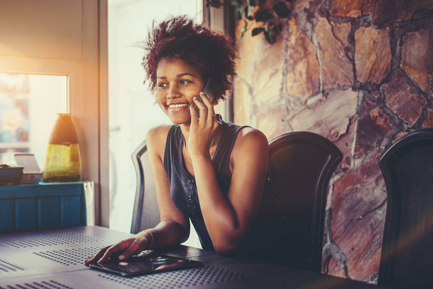 Cheerful black teenage female talking on the phone indoors - Photo, image
