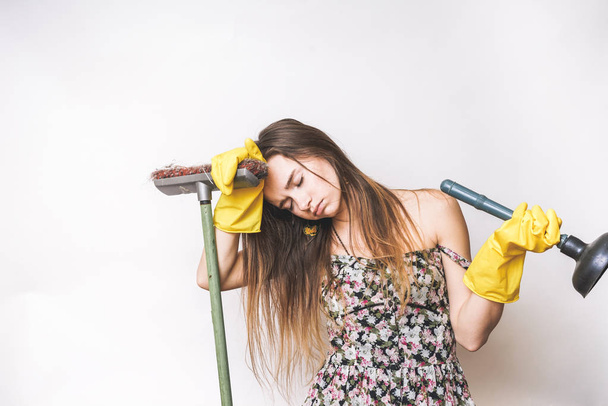 a tired young girl in yellow rubber gloves holds a plunger and a brush, is tired after cleaning - 写真・画像