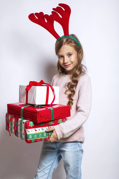 Happy little smiling girl with christmas gift box.Happy little smiling girl with christmas gift box.Christmas concept. Smiling funny girl in deer horns in studio. - Фото, зображення