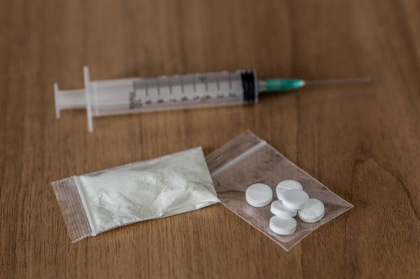 spoon, plastic packet with cocaine and syringe on the wooden table - Photo, Image