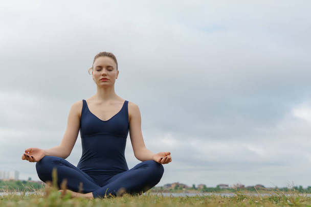 Mladá atraktivní dívka cvičí jógu, sedí v polovičním lotosu cvičení Ardha Padmasana pozice. - Fotografie, Obrázek
