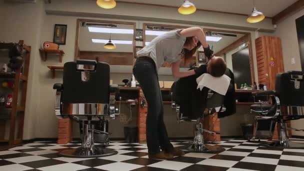 La mujer es una peluquera profesional baja la silla, la cámara se mueve con la ayuda de imágenes de HD Steadicam prístina. Peluquero en la barbería comienza a afeitar al hombre con la cuchilla
. - Imágenes, Vídeo