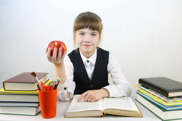 Schoolgirl in uniform with book and red apple smiles sitting - Φωτογραφία, εικόνα