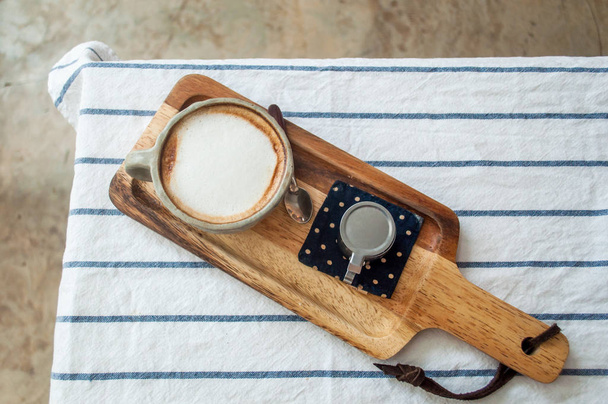 Café caliente con leche en la mesa de ropa a rayas sobre el piso de piedra
 - Foto, Imagen