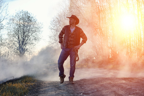 A man is wearing a cowboy hat and a loso in the field. American - Foto, imagen
