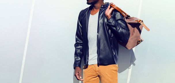 Fashion african man in a black leather jacket holds a bag in the - Фото, изображение