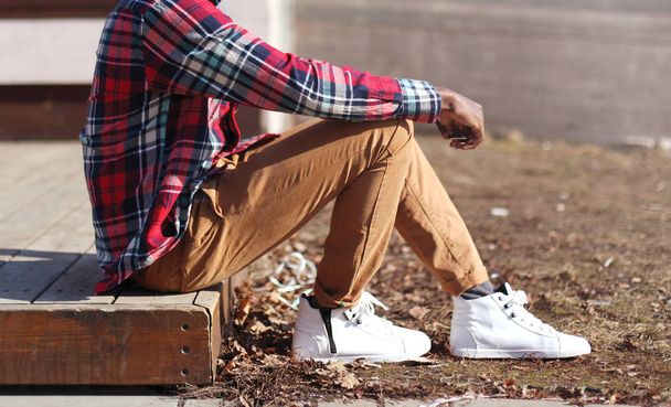 Fashion man in a plaid red shirt and casual sneakers sits in the - Foto, Imagem