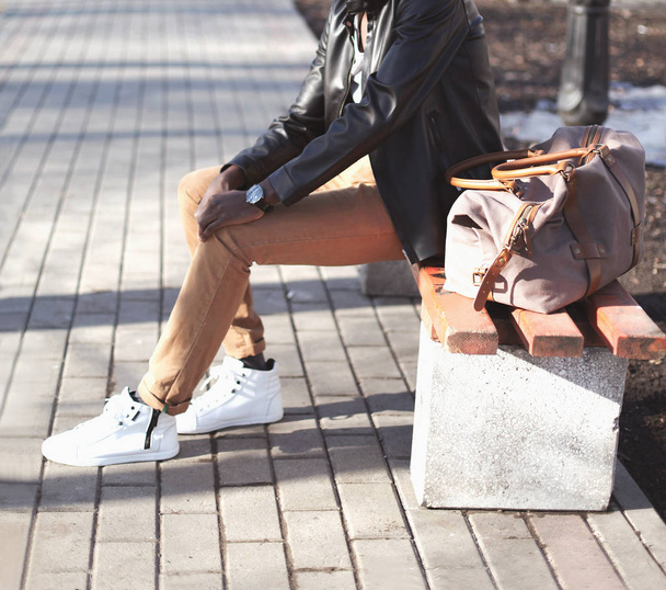 Fashion man with bag sits on a bench in the city park - Foto, imagen