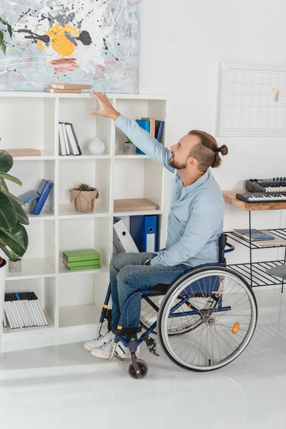 людина на інвалідному візку намагається дістатися до книги
 - Фото, зображення