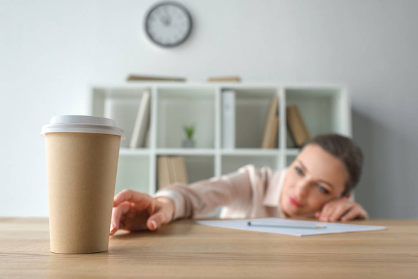 Businesswoman reaching for coffee in paper cup   - Foto, afbeelding