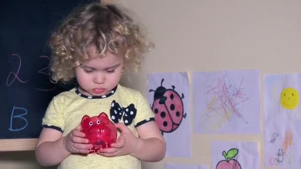 schönes Mädchen schüttelt Sparschwein mit Münzen darin - Filmmaterial, Video
