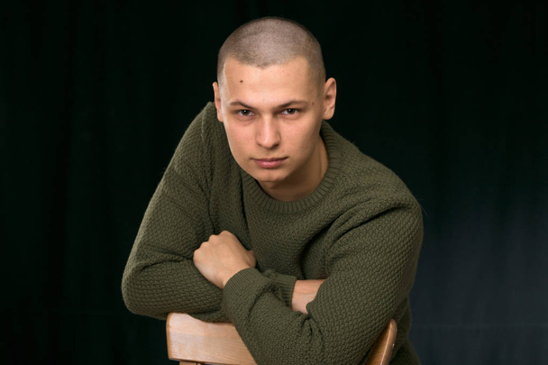 Ένας νεαρός άνδρας είναι σκίνχεντ σε ένα πουλόβερ πράσινο στρατιωτικό στυλ. στούντιο. - Φωτογραφία, εικόνα