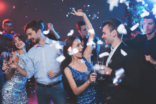 Νέοι άνθρωποι έχουν διασκέδαση σε ένα Πρωτοχρονιάτικο πάρτι. Σε πρώτο πλάνο χορεύουν δύο ζεύγη. - Φωτογραφία, εικόνα