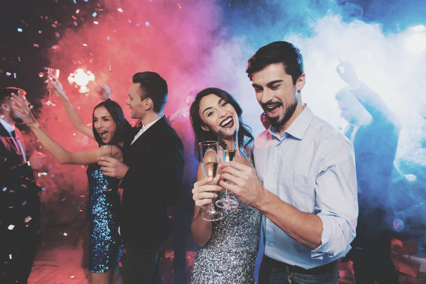 Young people have fun at a New Year's party. In the foreground, a couple is dancing with glasses in their hands. - Foto, Imagen