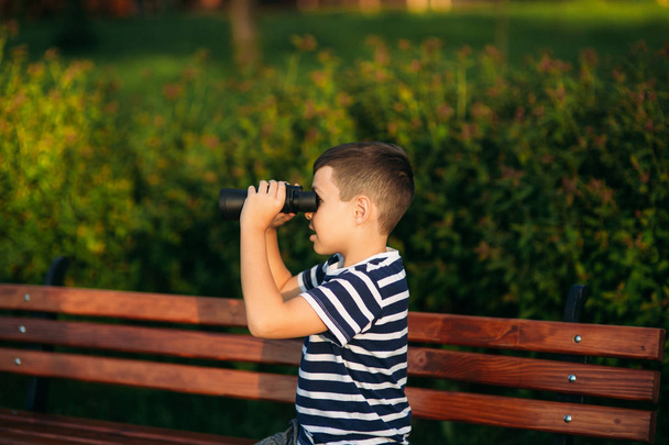 Jongetje in een gestreepte t-shirt kijkt door een verrekijker. Lente, zonnig weer. - Foto, afbeelding