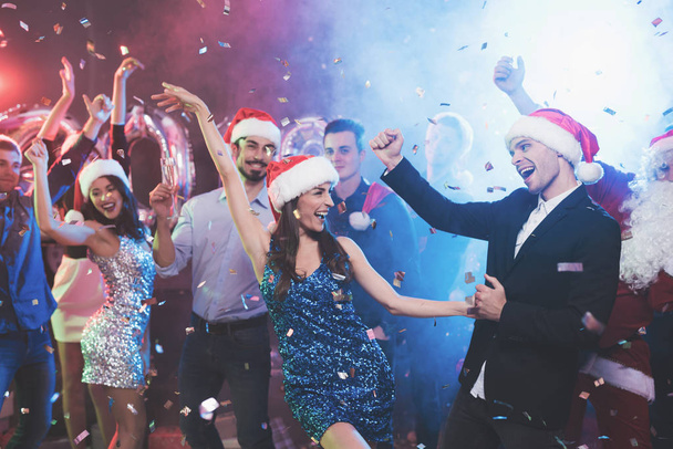 Νεαρό ζευγάρι έχει τη διασκέδαση στο πάρτι της Πρωτοχρονιάς. Χορεύουν στα καλύμματα του Αϊ-Βασίλη. - Φωτογραφία, εικόνα