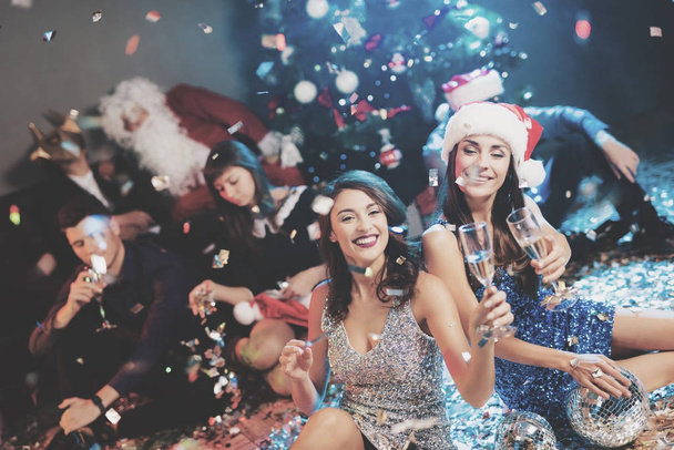 Two girls are sitting on the floor. Around them is scattered confetti. They rest after the party for the new year - Fotó, kép