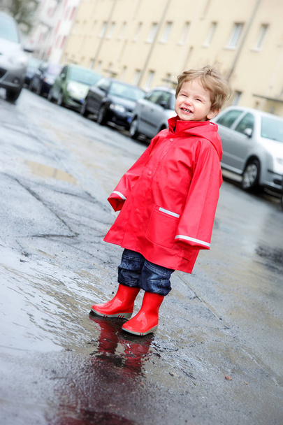 Little Boy in Red Rain Clothes having fun in Puddles outside on a Street in Berlin - Foto, immagini