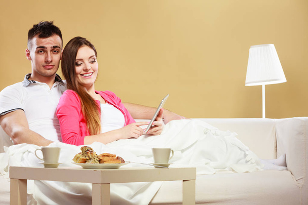 Couple reading ebook relaxing at home on sofa. - Фото, изображение