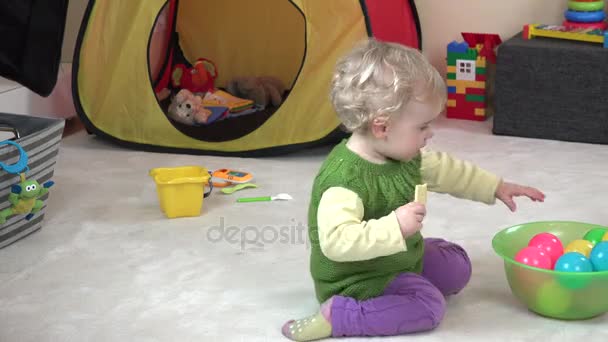 Batole dívka jíst cookie a hrát s barevnými míčky v herna. - Záběry, video