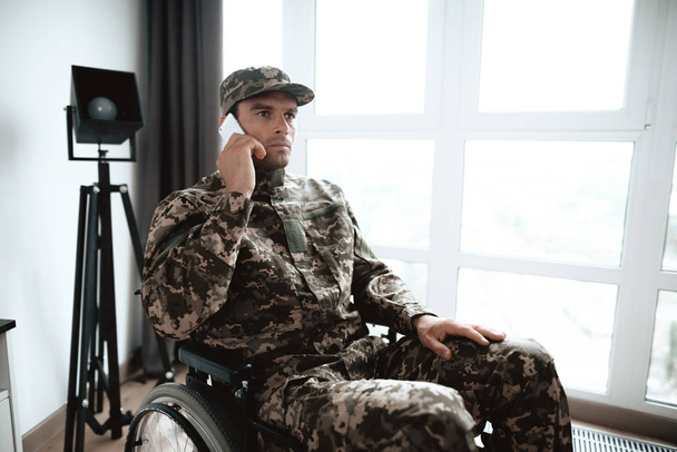 A fogyatékkal élők, a katonai egyenruha ül egy tolószék, egy nagy panoráma ablak. - Fotó, kép