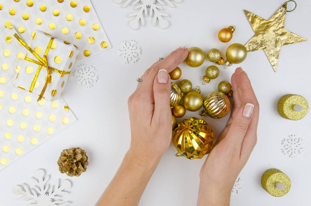 Mädchen halten goldene Weihnachtskugeln auf weißem Hintergrund mit Weihnachtsschmuck und Vorbereitung für die Feiertage, Dekoration für Weihnachtsbaum. weißer Hintergrund flach, von oben gesehen Weihnachten flach - Foto, Bild