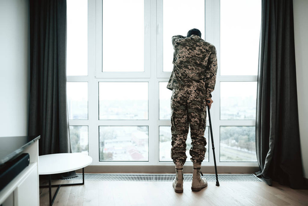 A disabled soldier stands with his hand on the window. He feels sad and depressed. - Фото, зображення