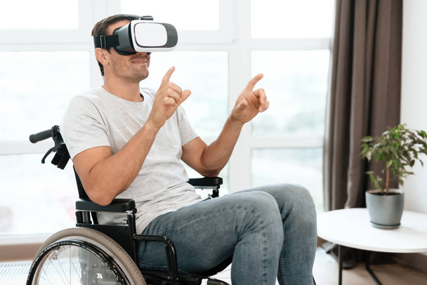 The disabled person is sitting in a wheelchair in virtual reality glasses. He spread his hands to the sides. - Fotoğraf, Görsel