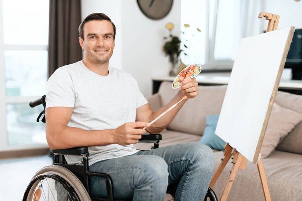 The disabled person is sitting in a wheelchair opposite the easel. He draws a picture. - Foto, imagen