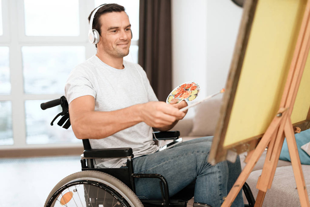 The disabled person is sitting in a wheelchair opposite the easel. He draws a picture. - Foto, Imagen