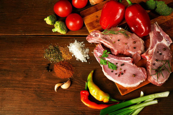Surowe steki, kotlety, mięso z przyprawami i warzywami na drewnianym stole - Zdjęcie, obraz