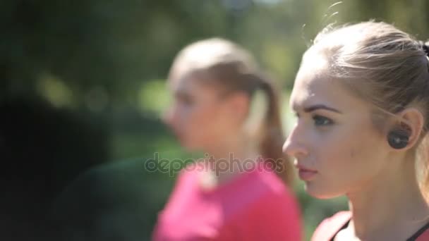 Dos chicas con auriculares inalámbricos se dedican a la cultura física en el parque. Ventajas de las tecnologías modernas
. - Metraje, vídeo