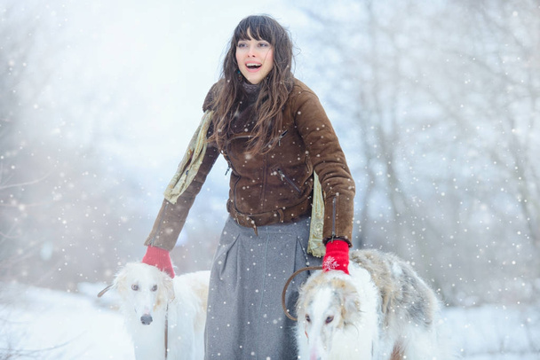 Christmas walk.  Beautiful surprised woman in winter clothes with greyhound dogs stylish winter background with snow, emotions.  portrait of a woman.  New Year - Photo, Image