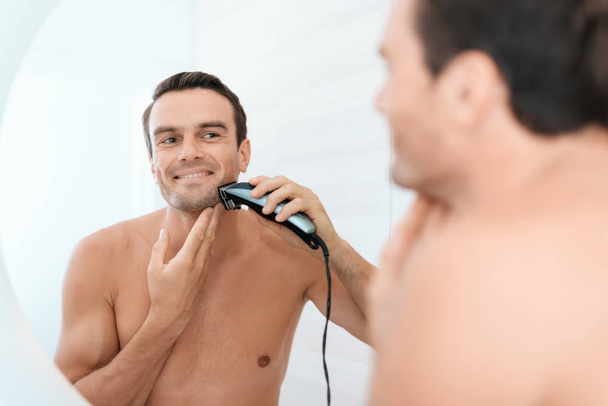 A man in the bathroom in the morning. He shaves the electric shaver in front of the mirror. - Photo, image