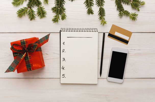 Prepárate para Navidad, año nuevo. Lista de deseos, teléfono, tarjeta de crédito, regalo sobre fondo de tabla de madera blanca
 - Foto, imagen