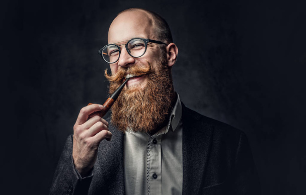Close up portrait of shaved head aristocratic male in eyeglasses smoking pipe over grey background. - Photo, Image