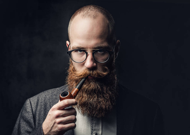 Retrato de cerca de cabeza afeitada aristocrático macho en gafas fumar pipa sobre fondo gris
. - Foto, Imagen
