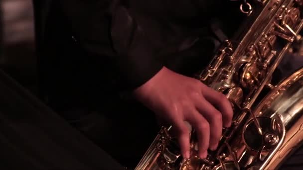 De hand van een man in een zwart pak op een gouden saxofoon in een jazzband. Close-up. - Video