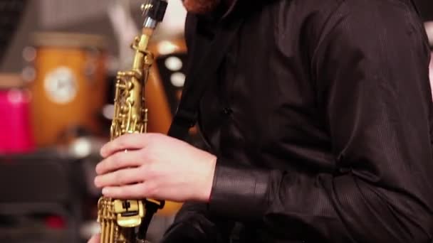 Een man met een baard in een zwart shirt speelt emotioneel sopraansaxofoon. Close-up. - Video