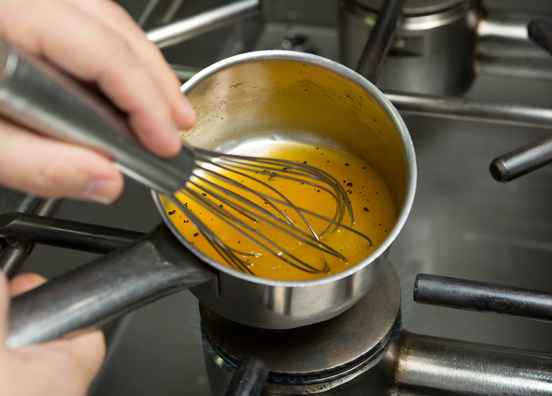 A metal mixing bowl full of fresh chicken stock being reduced over a flaming hob.The chicken stock is being whisked by hand and whisker - Foto, imagen