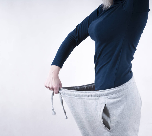 Una mujer muestra una pérdida de peso usando pantalones grandes viejos. El concepto de pérdida de peso
 - Foto, imagen