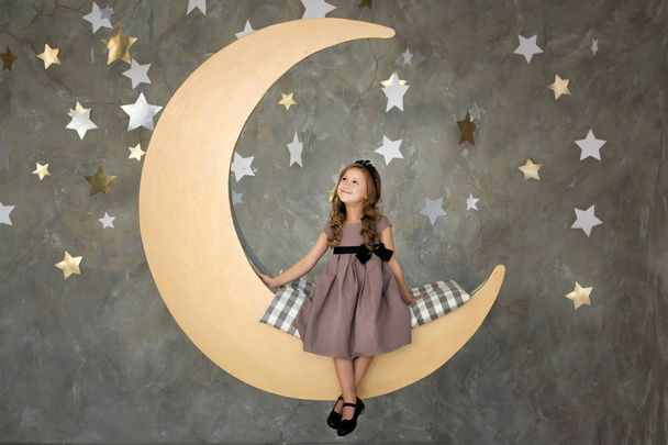 klein meisje in het zittend op grote maan. Meisje droomt - Foto, afbeelding