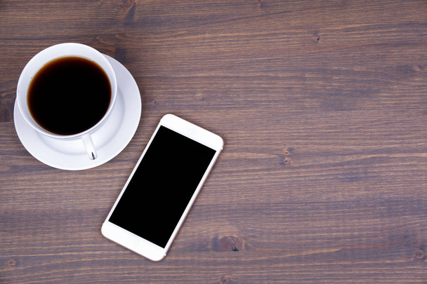 Bovenaanzicht van een kopje koffie met slimme telefoon op houten achtergrond - Foto, afbeelding